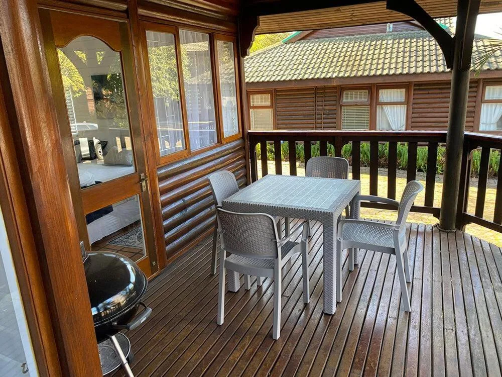 Covered wooden deck with dining table, chairs, and braai grill