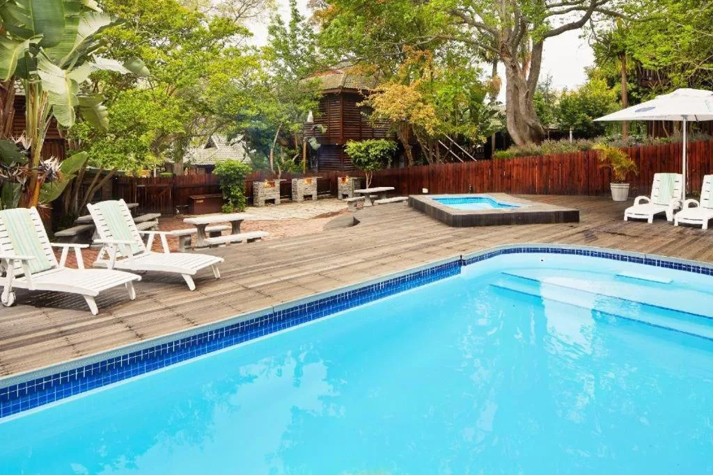Crystal blue swimming pool with wooden deck, loungers, and second pool beyond