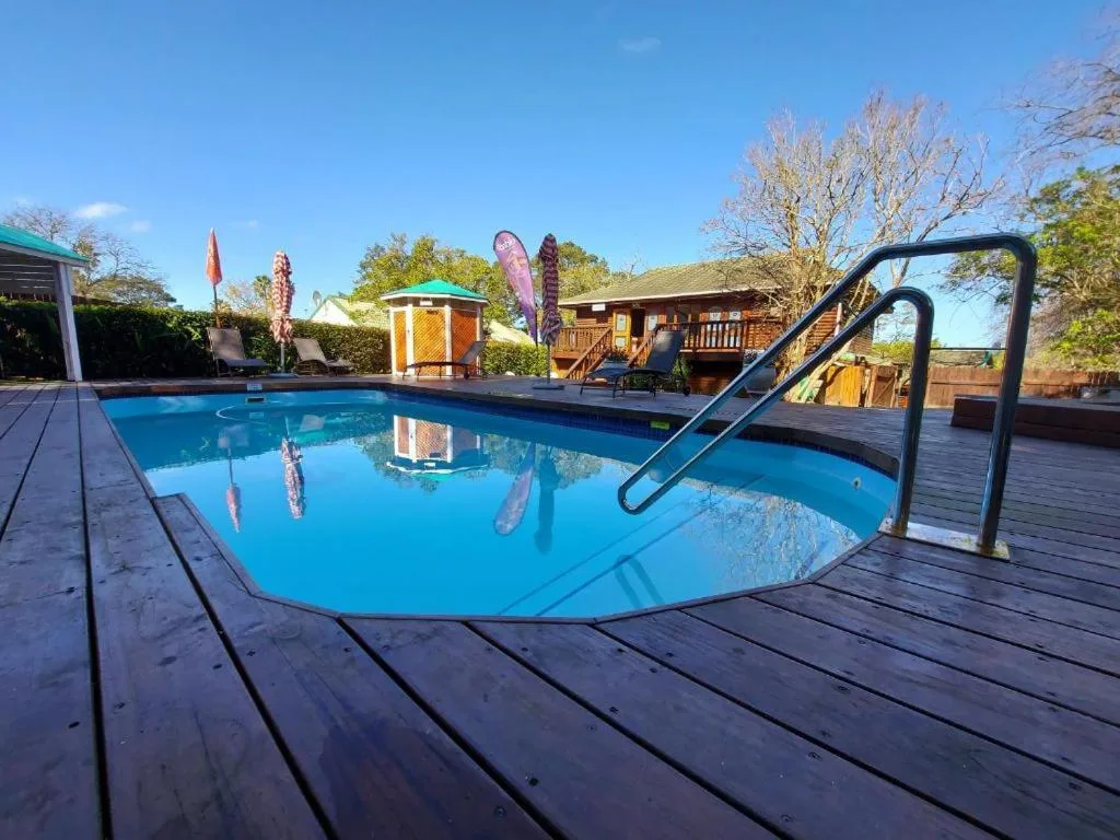Blue swimming pool with wooden deck, metal ladder, and lush garden surroundings