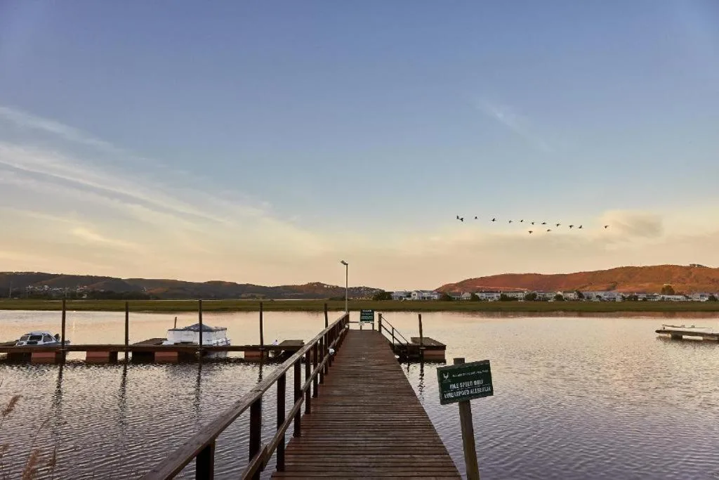 Wooden jetty extending into calm lagoon with moored boats and distant hills