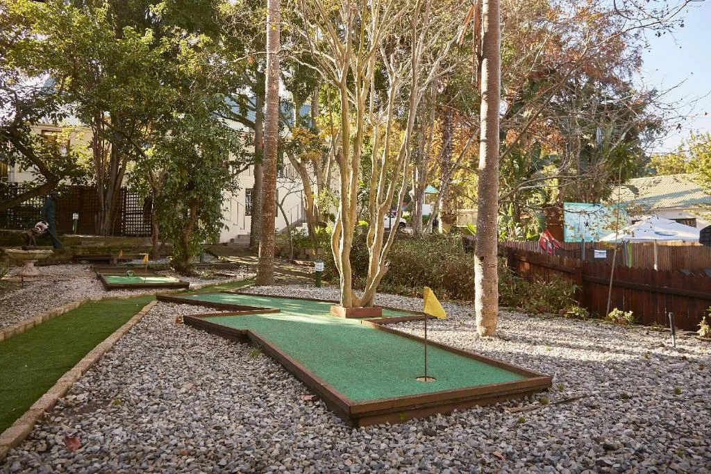 Miniature golf course with multiple green holes set under tall trees