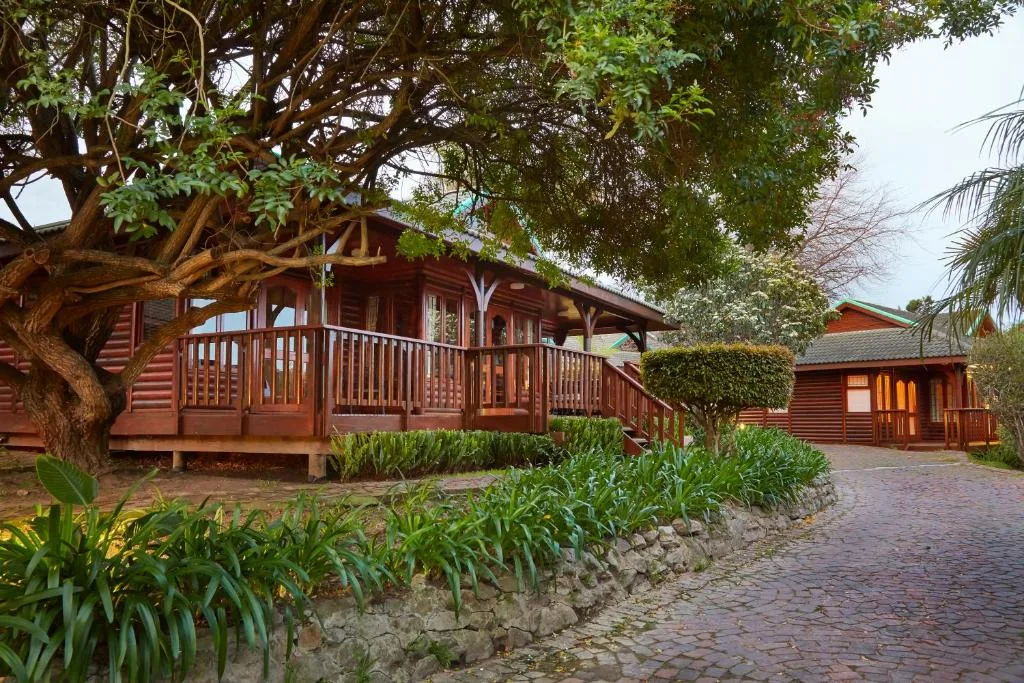 Red timber lodge with wooden deck under sprawling trees and manicured gardens