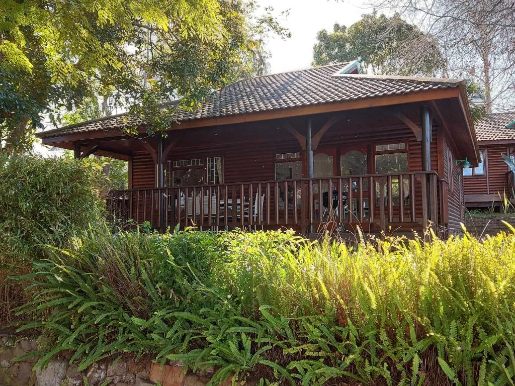 Wooden cabin with covered deck surrounded by lush green gardens and trees