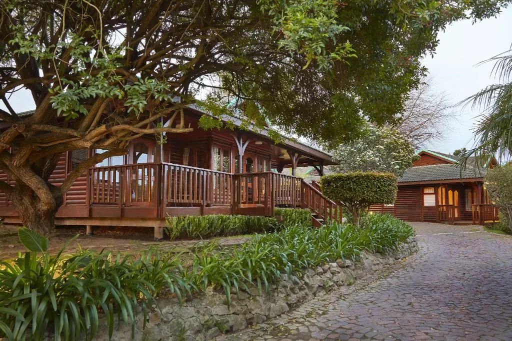 Red-painted timber cottage with wraparound deck and manicured garden entrance