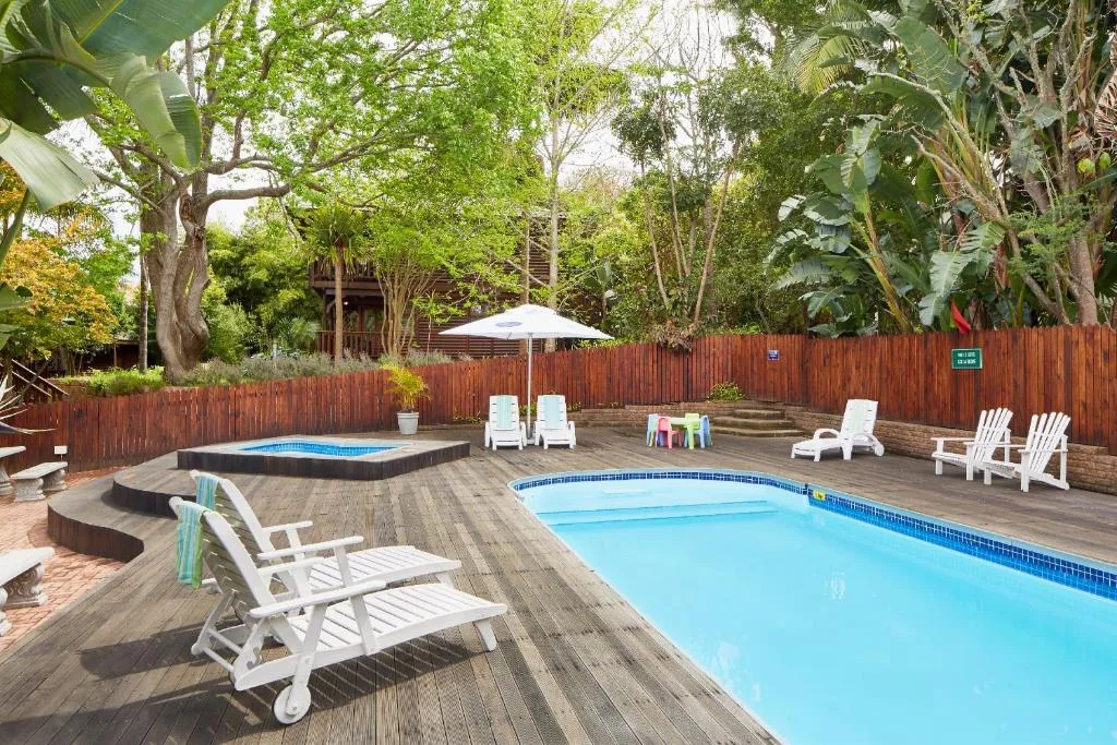 Swimming pool with loungers, umbrella, and lush garden trees surrounding