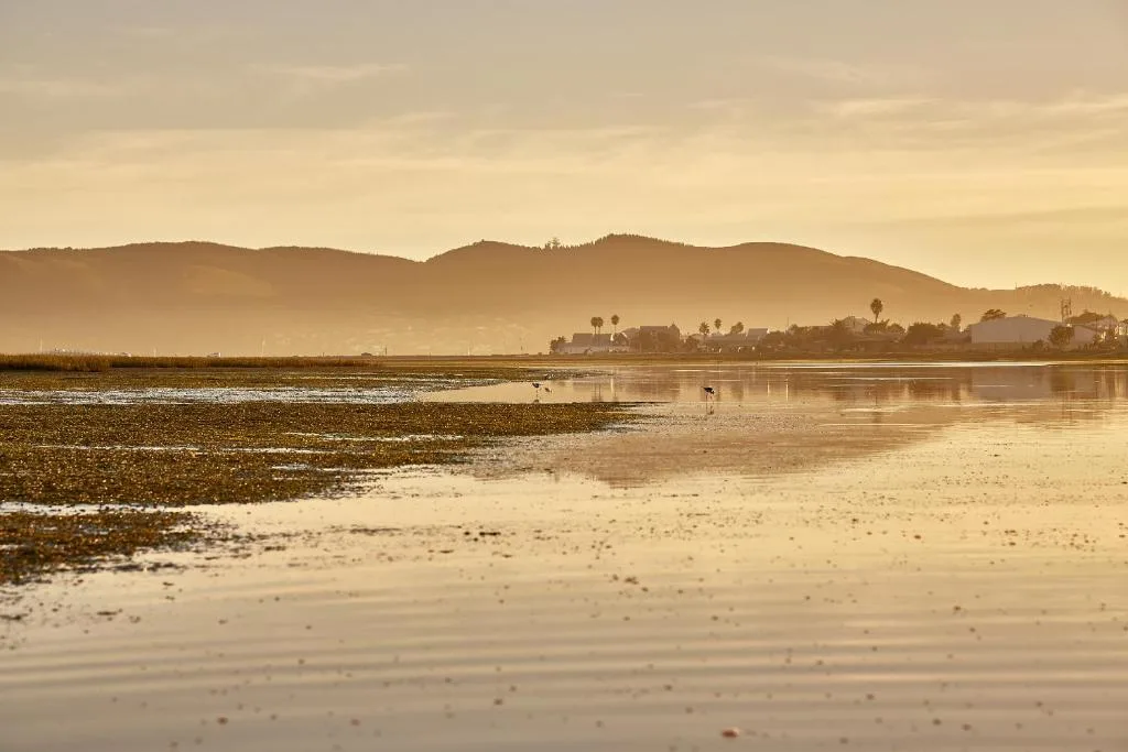 Golden sunrise over lagoon with mountains and distant property across water