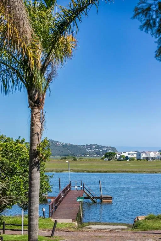 Lagoon view with wooden jetty, palm trees, and distant hillside homes