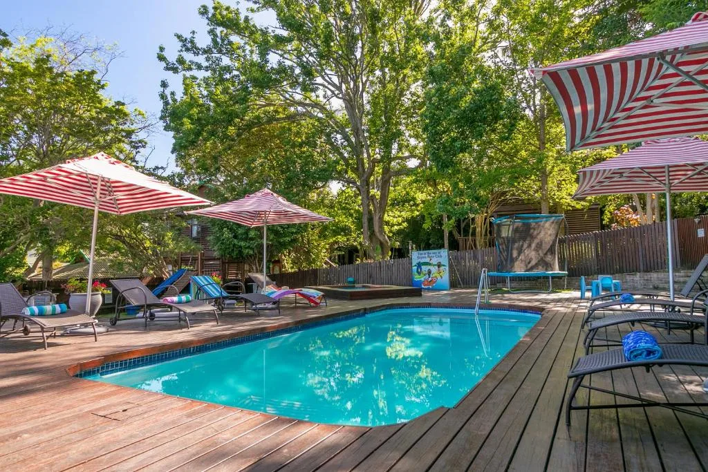 Sparkling swimming pool with striped umbrellas and wooden deck surrounding it