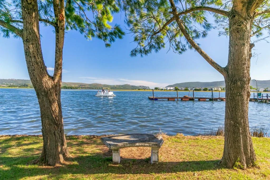 Scenic lagoon view with boats, mountains, and bench seating under trees