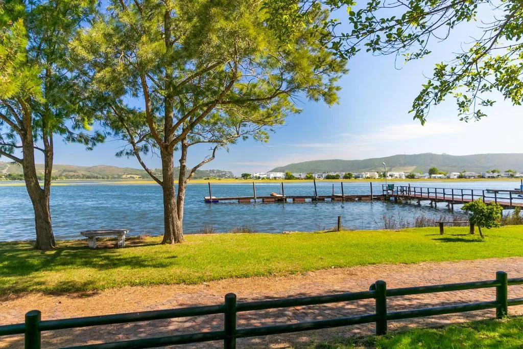 Scenic lagoon view with mountains, boats, and green lawn framed by trees