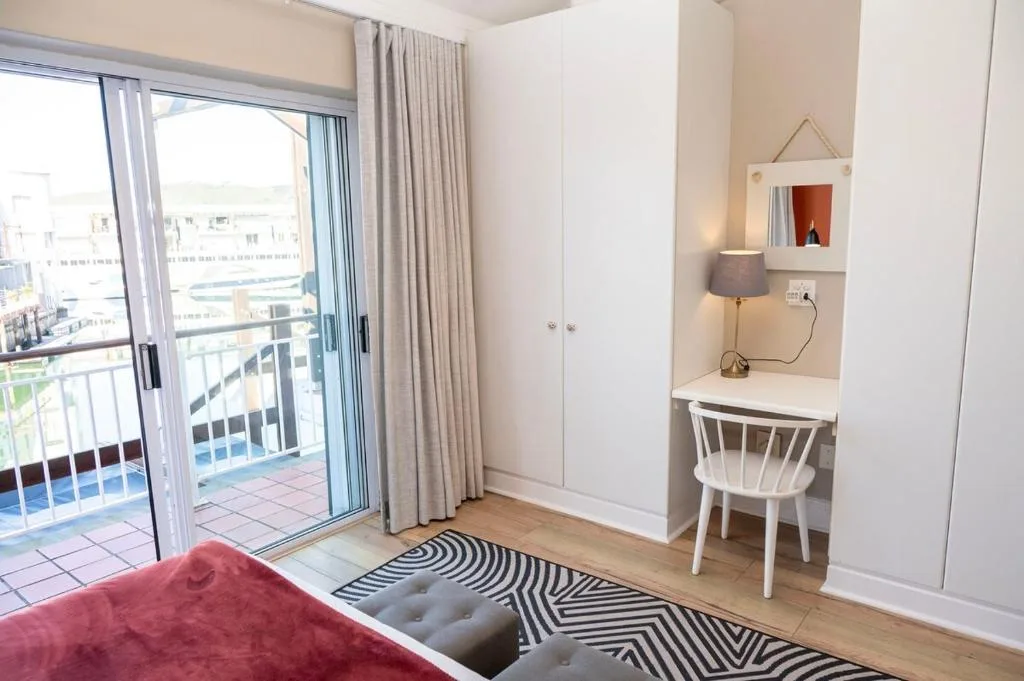 Modern bedroom with balcony view, desk area, and waterfront lagoon scenery