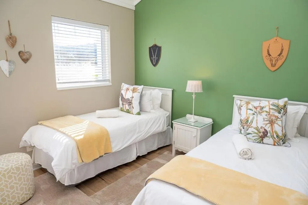 Bright bedroom with two single beds, green accent wall, and natural light from window