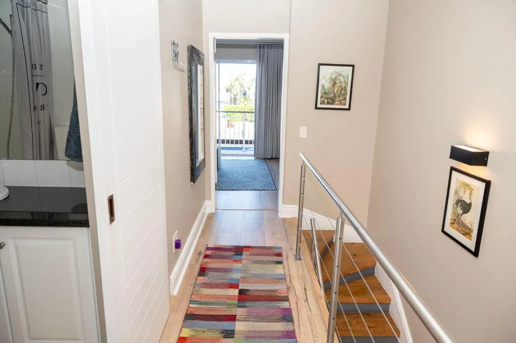 Modern hallway with wooden stairs, colorful runner rug, and framed art