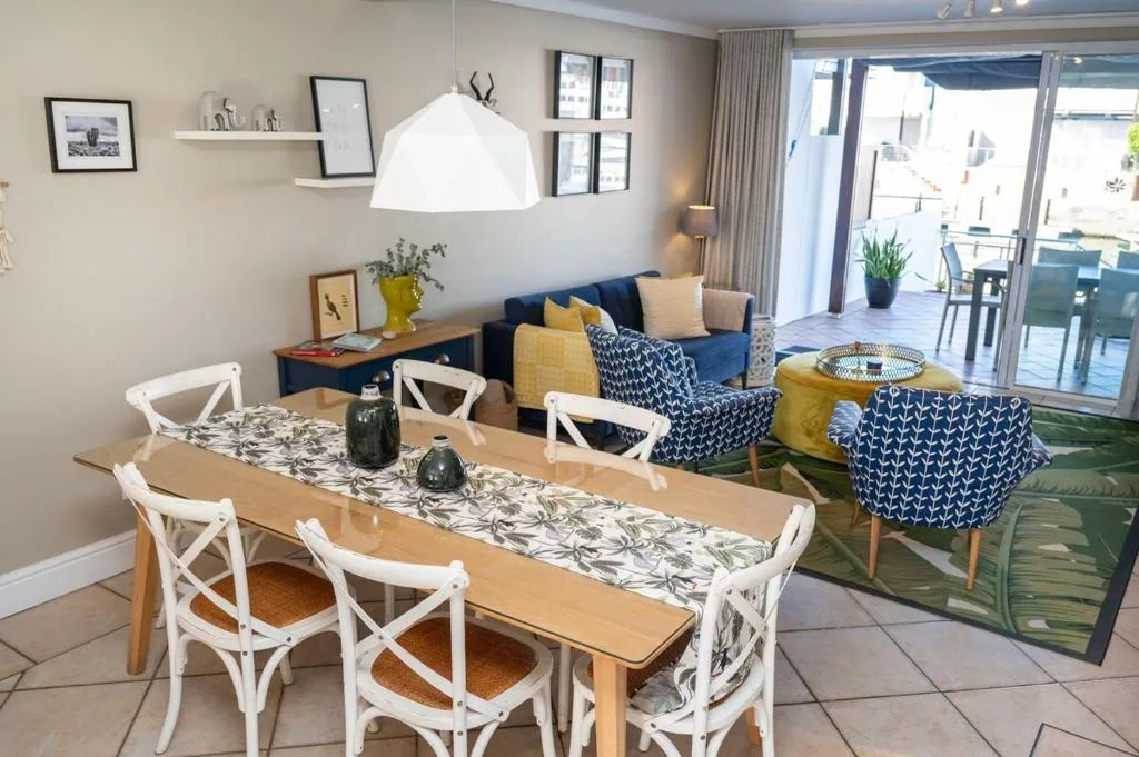 Modern dining table with white chairs and botanical runner, overlooking lounge area