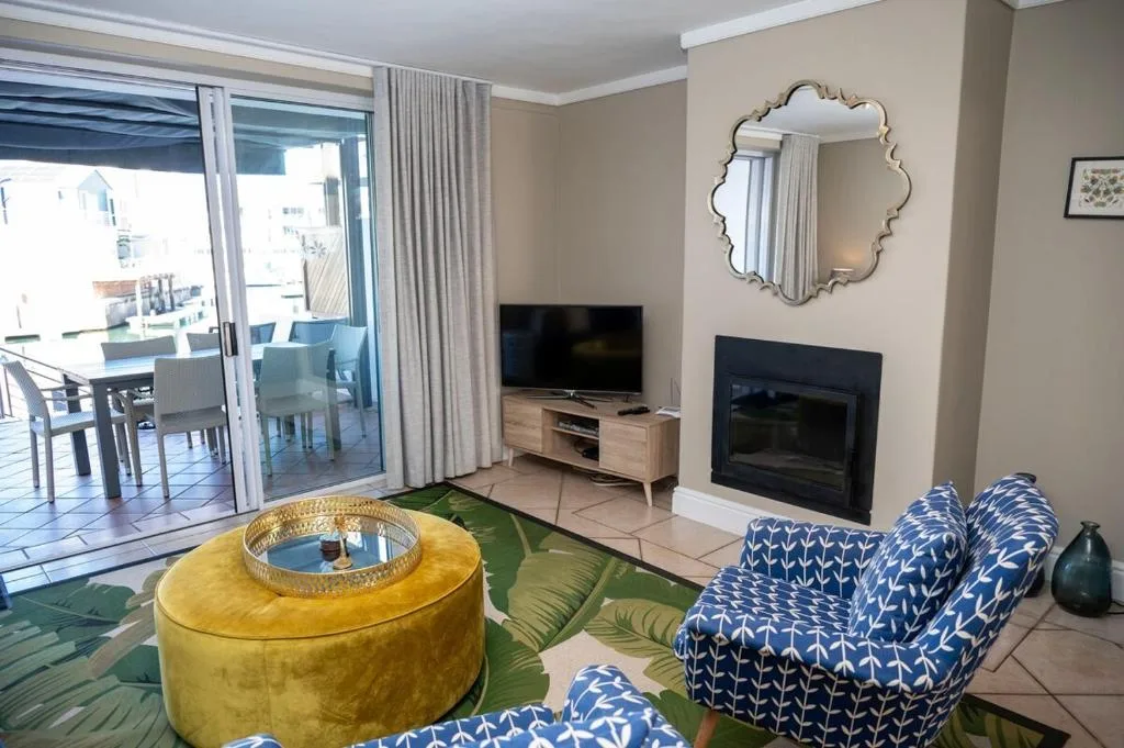 Modern lounge with blue patterned sofa, yellow ottoman, fireplace, and lagoon views
