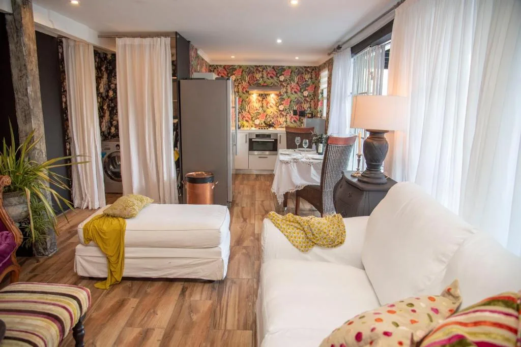 Bright bedroom with two white beds, colorful bedding, and kitchen visible