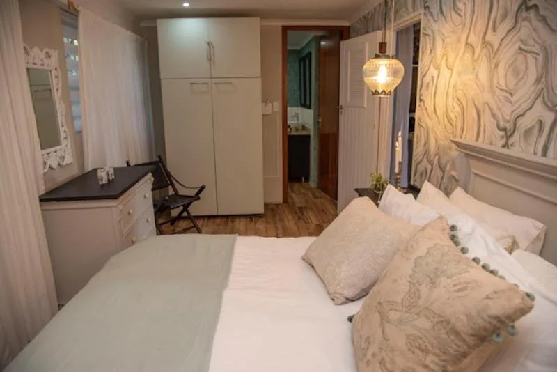Bright bedroom with queen bed, white linens, decorative pillows, and ensuite access