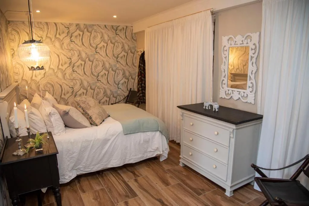 Elegantly furnished bedroom with patterned wallpaper, white bedding, and dark wood furniture