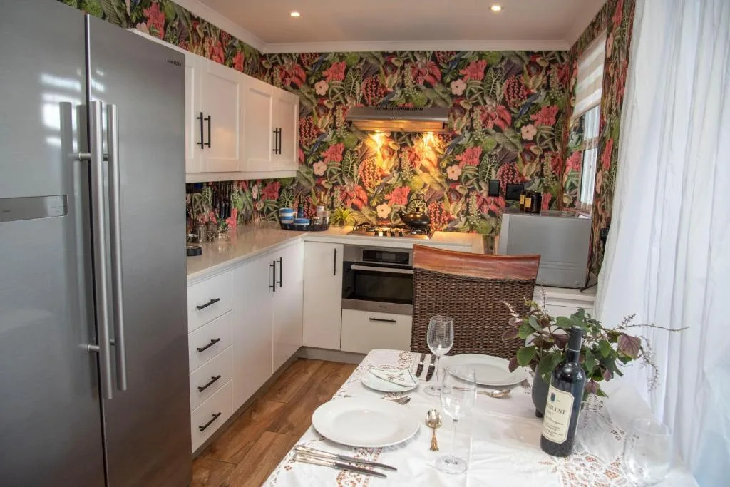 Modern white kitchen with floral wallpaper, stainless steel appliances, and dining setup