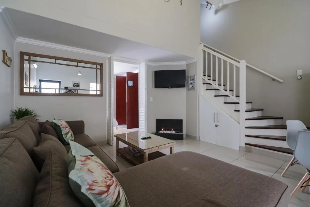Open-plan lounge with brown sofa, fireplace, TV, and wooden staircase