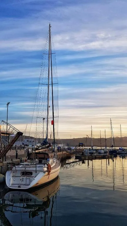 Sailboats moored in calm Knysna Lagoon at sunrise with mountains beyond