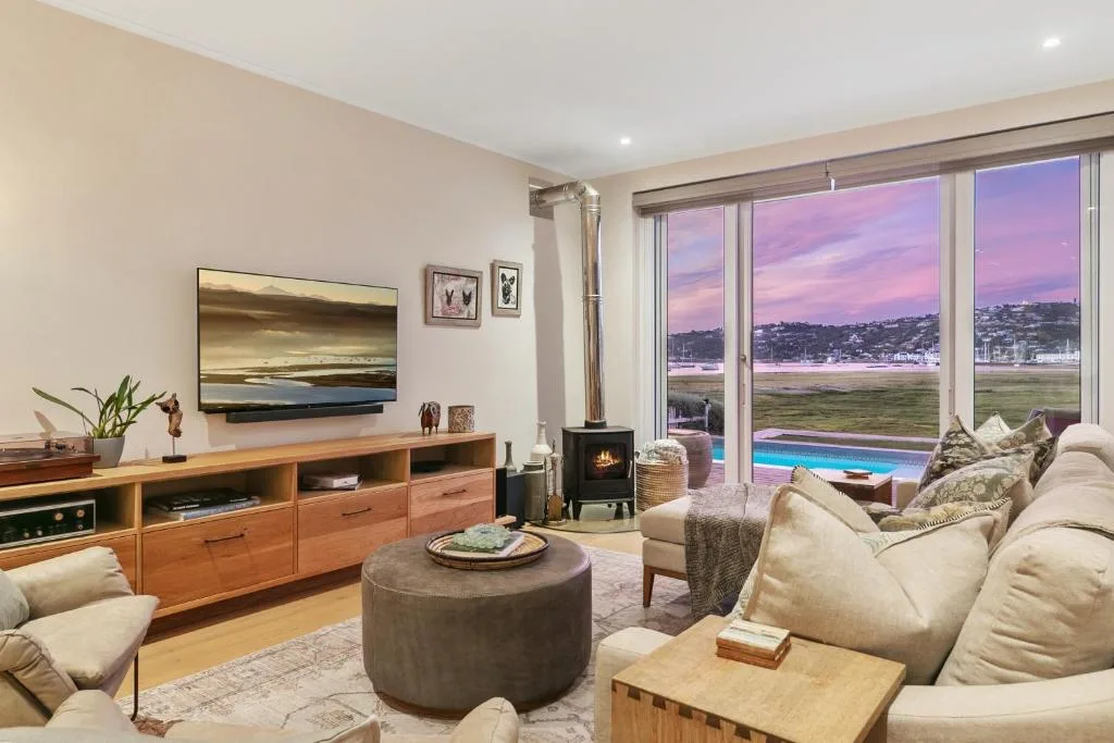 Spacious lounge with cream sofas, wooden media unit, fireplace, and lagoon views