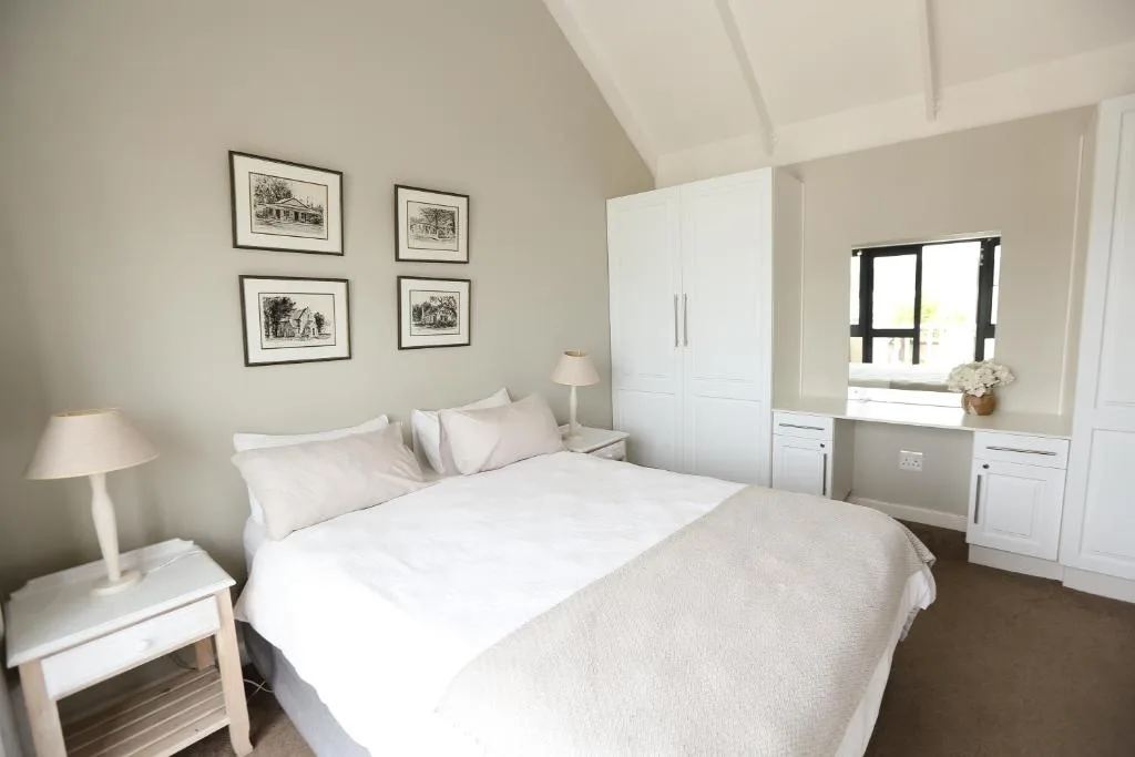 Bright, airy bedroom with white bedding, wardrobe, and framed artwork on walls