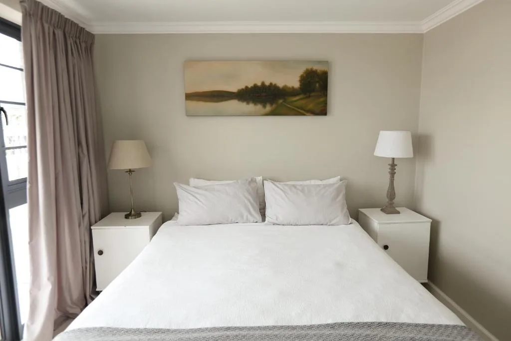 Bedroom with white bed, matching nightstands, table lamps, and landscape artwork