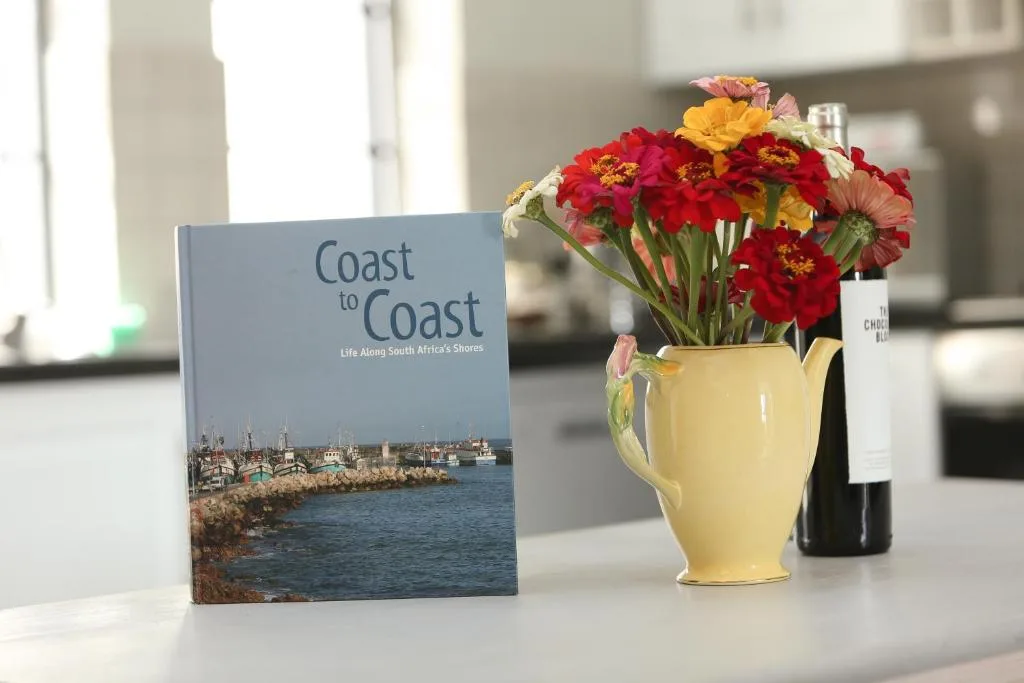 Colorful flowers in yellow pitcher with book and wine bottle on counter