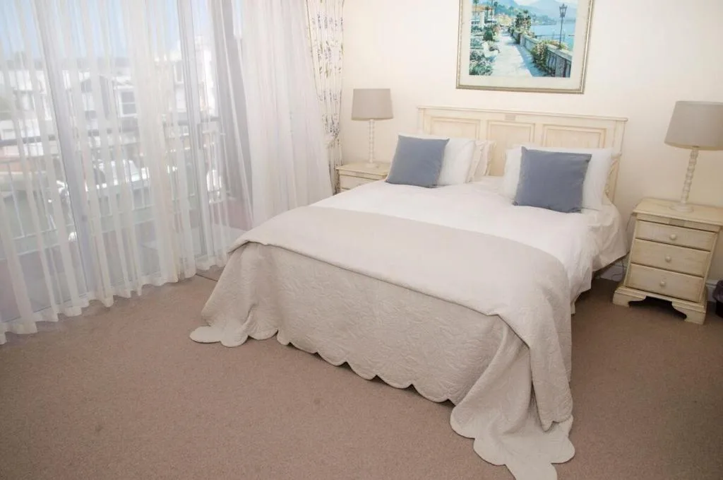 Spacious bedroom with queen bed, cream bedding, blue accent pillows, and lagoon view artwork
