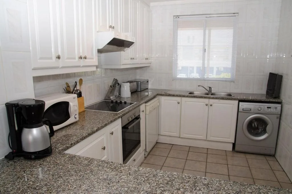 Bright white kitchen with granite counters, stove, and washing machine