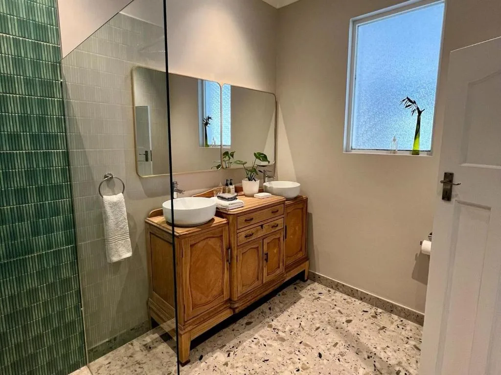 Modern bathroom with dual vanity, green tile shower, and natural light