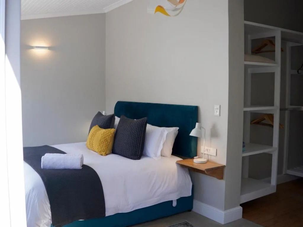 Neat bedroom with teal headboard, white linens, colorful pillows, bedside lamp