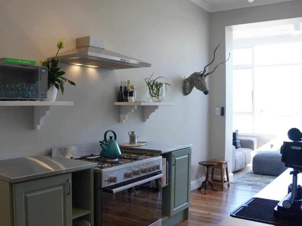 Modern kitchen with stove, hood, open shelving, and sage green cabinetry