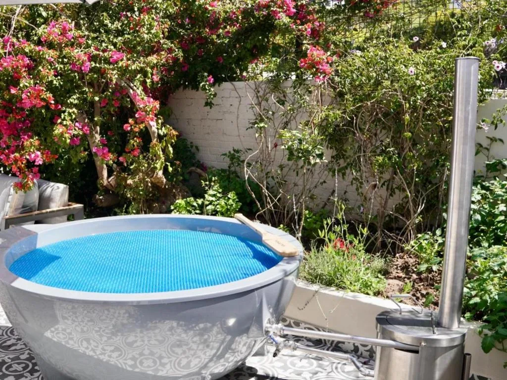 Round blue soaking pool nestled in lush garden with vibrant pink bougainvillea flowers