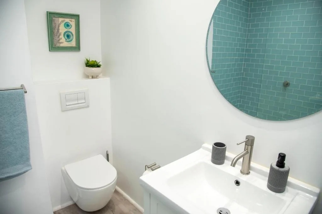 Modern bathroom with turquoise tiled mirror, white vanity, and toilet