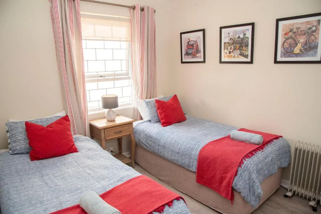 Twin bedroom with red accents, wooden bedside table, and bright window