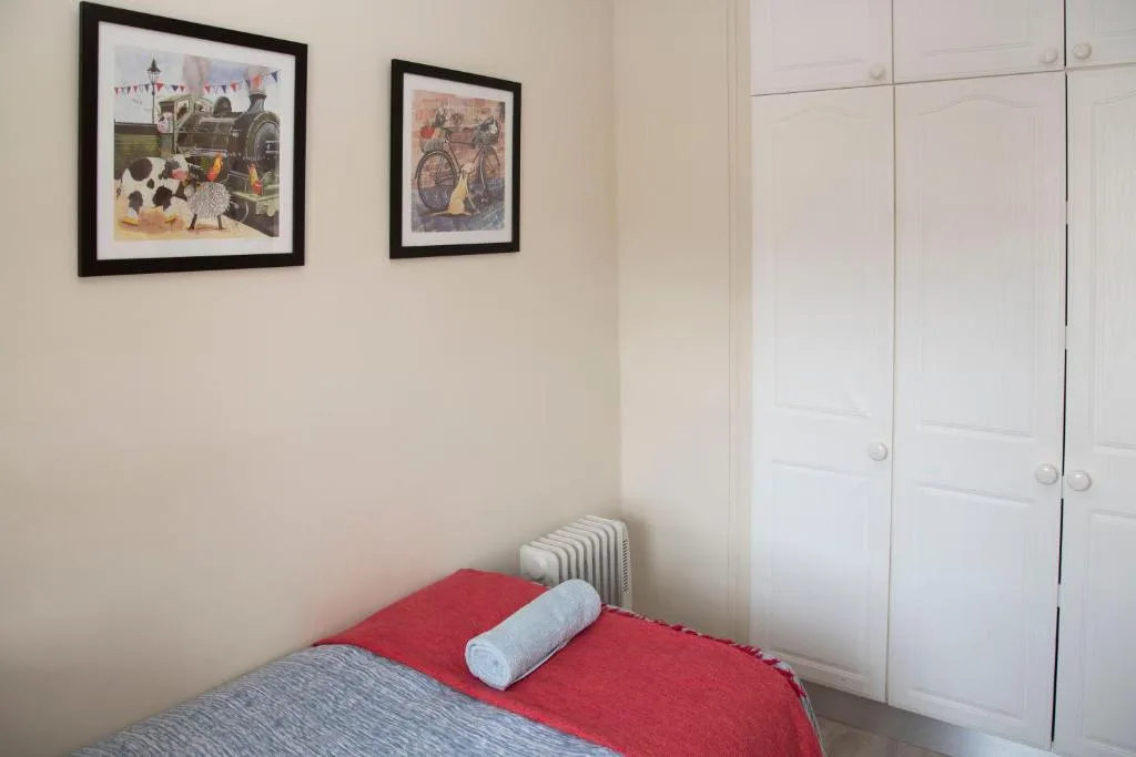 Bedroom with red bedding, white wardrobe, and framed artwork on walls