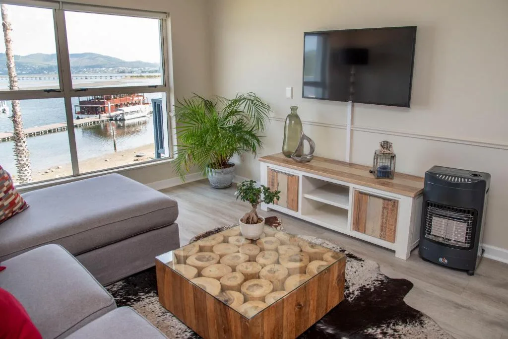 Living room with sofa, TV, and water views through large windows