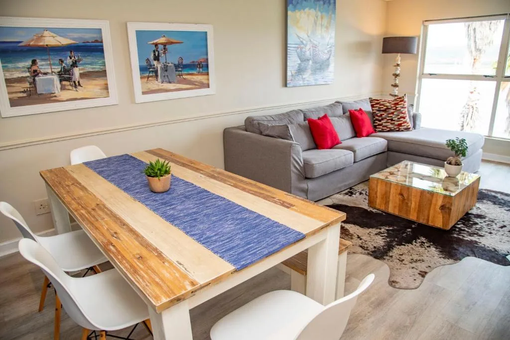 Open-plan lounge with gray sofa, dining table, and beach-themed wall art