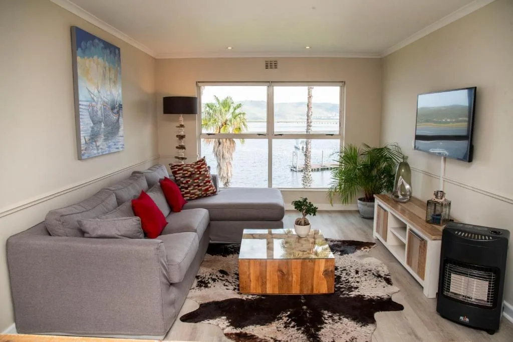 Spacious lounge with gray sofa, red cushions, water views through large windows