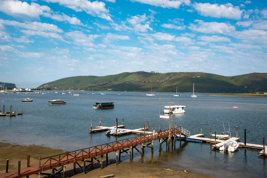 Scenic lagoon view with boats, jetty, and lush green hills under blue sky