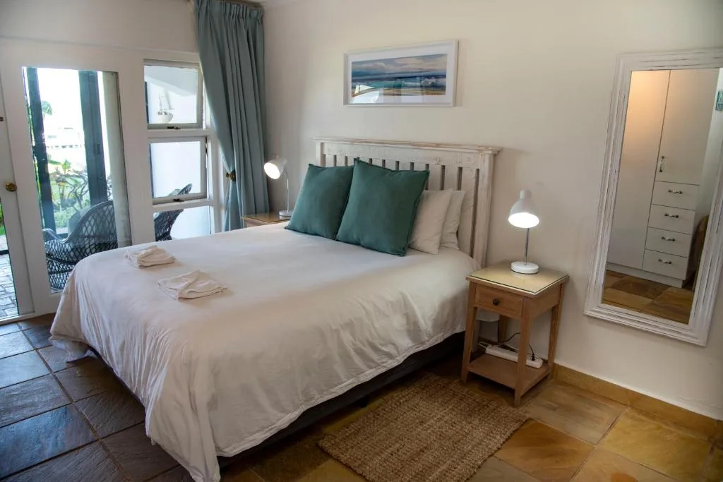Bright bedroom with queen bed, green pillows, and access to patio area