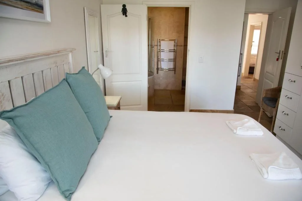Bright bedroom with queen bed, teal pillows, and ensuite bathroom access