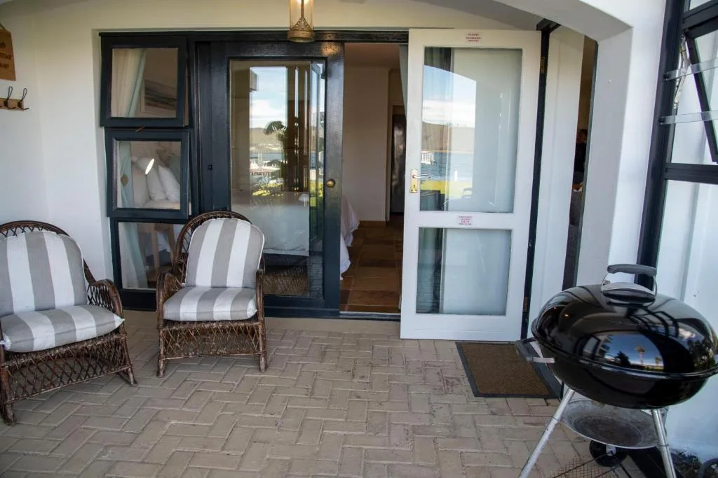 Covered patio with wicker chairs, braai grill, and glass doors opening indoors