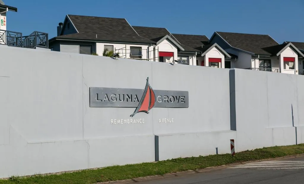 White boundary wall with Laguna Grove signage and residential buildings beyond
