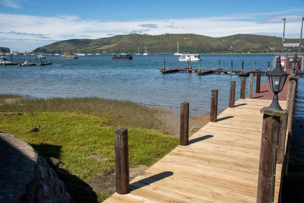 Scenic lagoon view with wooden jetty, boats, and green hillsides beyond