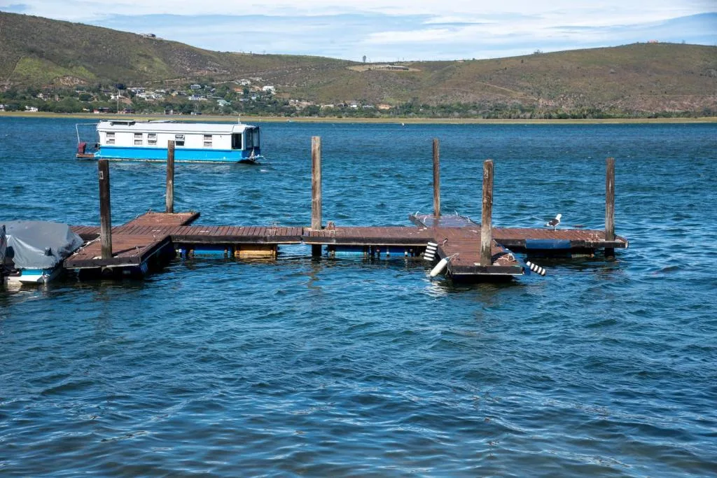 Scenic lagoon view with wooden jetty, moored houseboat, and green hillside backdrop