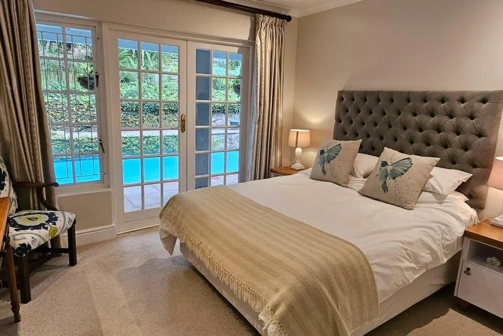 Spacious bedroom with upholstered headboard overlooking pool through glass doors