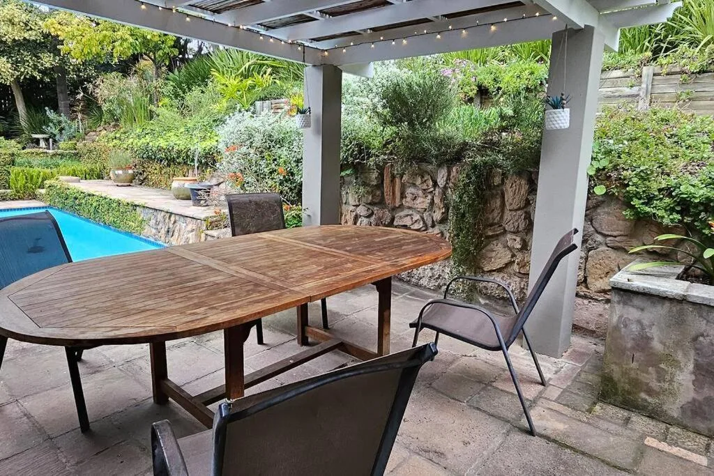 Covered patio with wooden dining table, chairs, and pool view